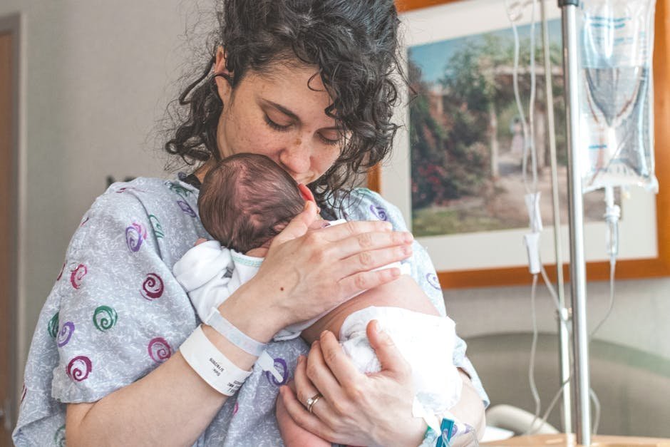 Mother holding newborn while attending virtual perinatal therapy session on laptop at home